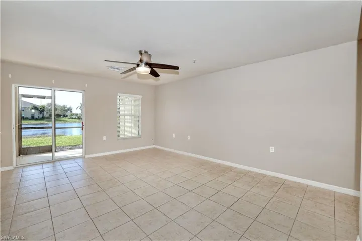 Unfurnished room with light tile patterned flooring, a ceiling fan, baseboards, and a water view