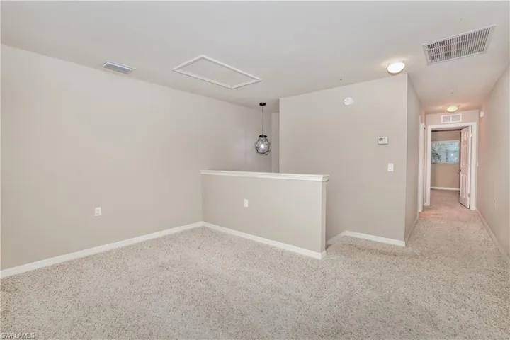 Carpeted spare room with attic access and baseboards