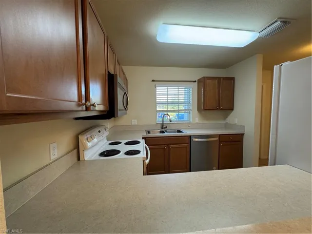 Kitchen featuring dishwasher, stove, a sink, light countertops, and brown cabinets