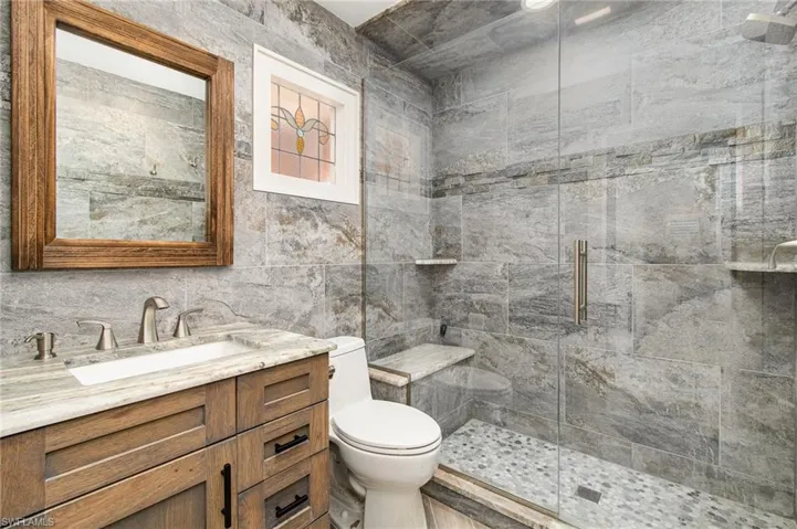 Guest Bathroom featuring toilet, a shower with shower door, vanity, and tile walls