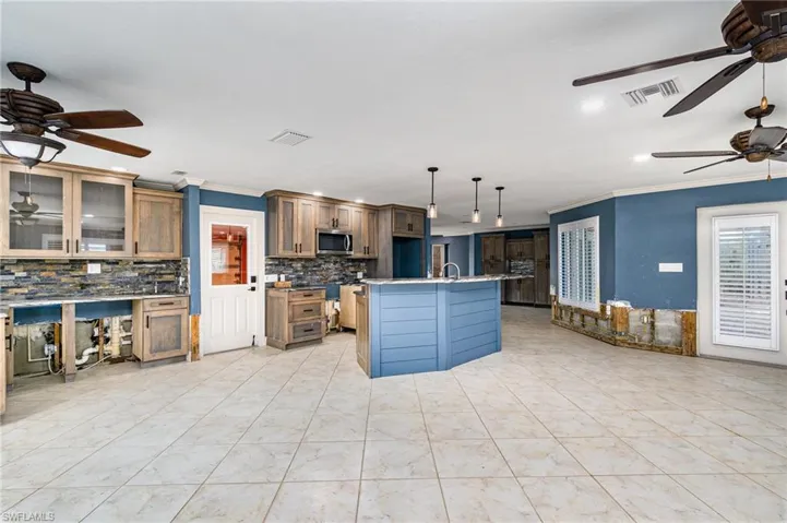 Kitchen with an island with sink, backsplash, sink, crown molding, and decorative light fixtures