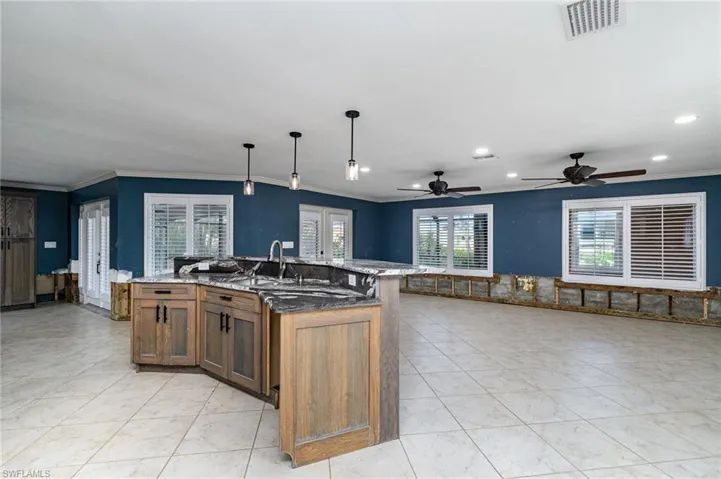 Kitchen featuring a large island with sink, crown molding, hanging light fixtures, and dark stone counters