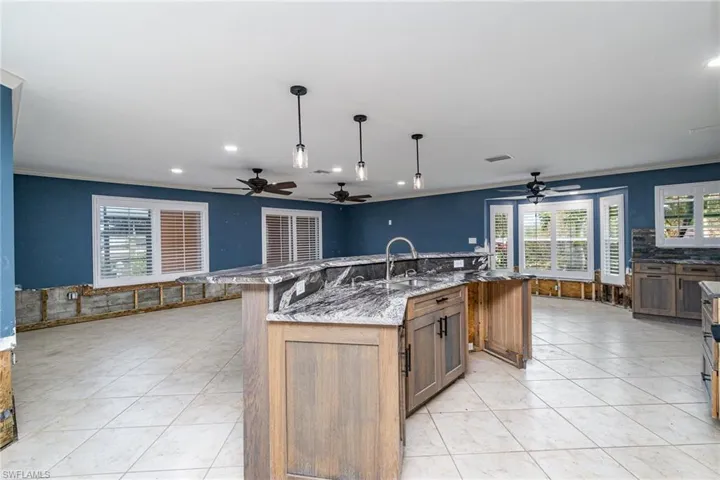 Kitchen with a large island, light stone countertops, ornamental molding, pendant lighting, and sink