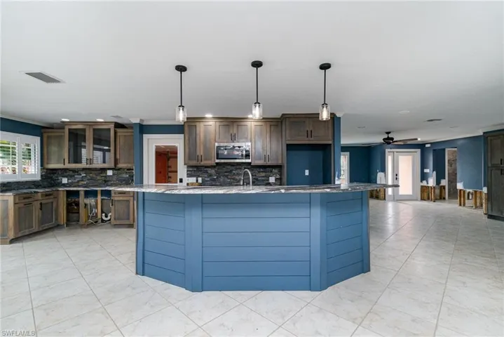 Kitchen featuring ceiling fan, decorative backsplash, a center island with sink, and hanging light fixtures