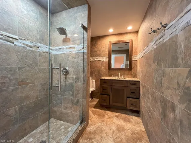 Outdoor Pool Bathroom featuring vanity, a shower with shower door, tile patterned floors, and tile walls