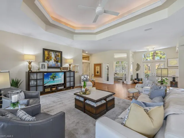 Living room with wood finished floors, baseboards, ornamental molding, ceiling fan, and a raised ceiling