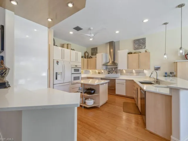 Kitchen with visible vents, wall chimney range hood, a peninsula, white appliances, and a sink