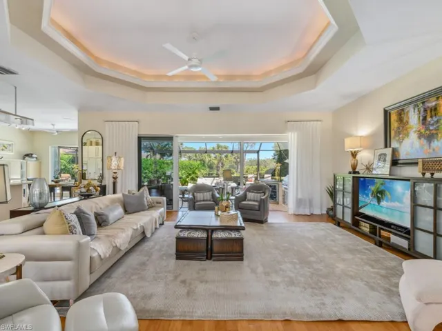 Living room with a raised ceiling, wood finished floors, a ceiling fan, and visible vents