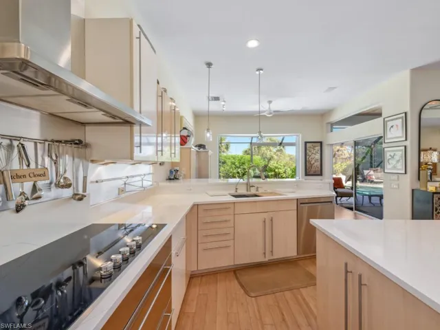 Kitchen featuring black electric stovetop, wall chimney range hood, light brown cabinetry, dishwasher, and a sink