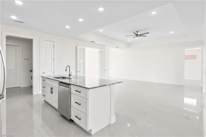 Kitchen with dark stone counters, a tray ceiling, a center island with sink, recessed lighting, and open floor plan