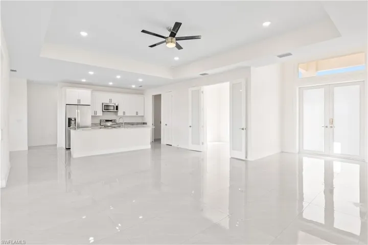 Unfurnished living room with a raised ceiling, recessed lighting, a ceiling fan, and french doors