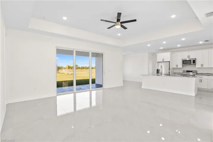 Unfurnished living room featuring a tray ceiling, recessed lighting, ceiling fan, and light tile patterned flooring