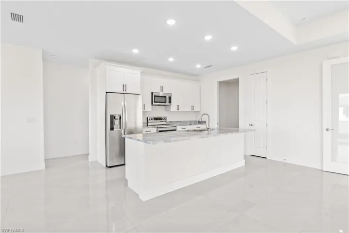 Kitchen with white cabinets, stainless steel appliances, light stone counters, recessed lighting, and a kitchen island with sink