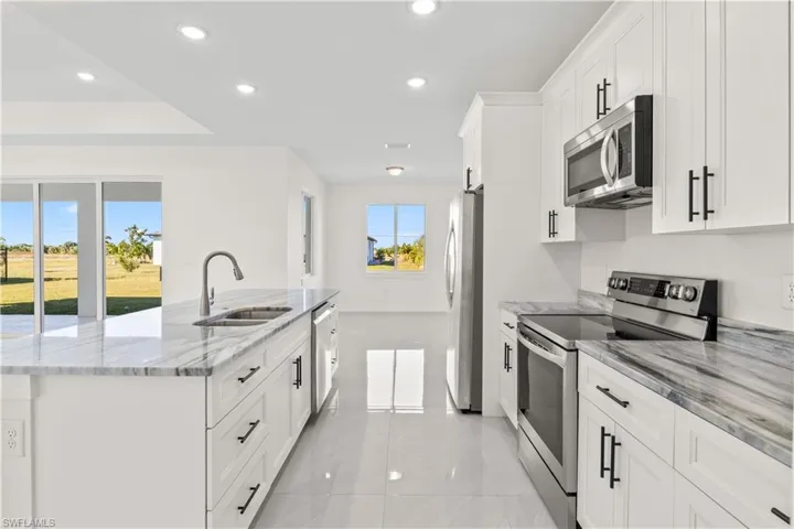 Kitchen with appliances with stainless steel finishes, a spacious island, light stone countertops, recessed lighting, and white cabinetry