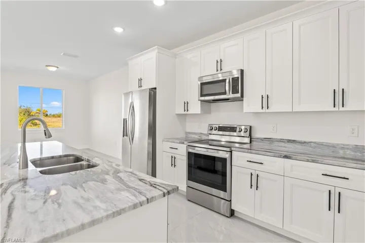 Kitchen with stainless steel appliances, light stone counters, white cabinets, recessed lighting, and light marble finish floors