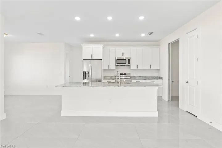 Kitchen featuring white cabinets, light stone counters, stainless steel appliances, a center island with sink, and recessed lighting