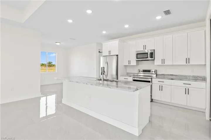 Kitchen with light stone countertops, an island with sink, white cabinets, stainless steel appliances, and recessed lighting