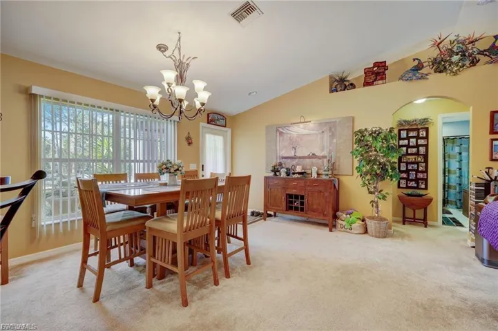 Dining space featuring light colored carpet, lofted ceiling, arched walkways, and a chandelier