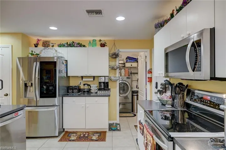 Kitchen with stainless steel appliances, white cabinetry, washer / clothes dryer, light tile patterned flooring, and dark countertops