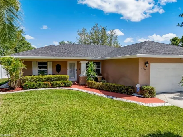Ranch-style home featuring a garage, a front lawn, stucco siding, and roof with shingles