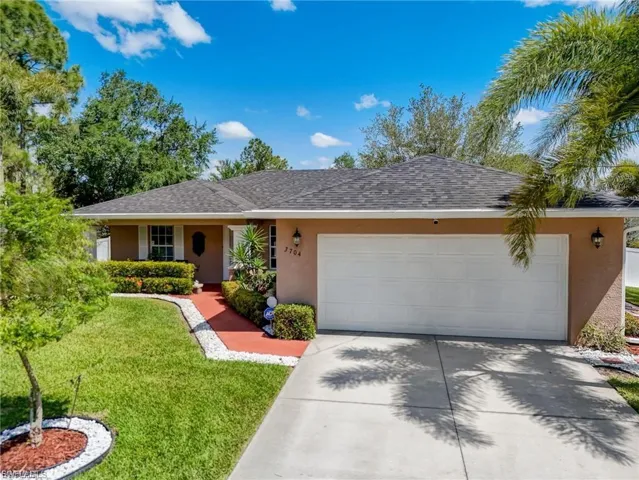 Ranch-style home with stucco siding, a front lawn, an attached garage, driveway, and roof with shingles