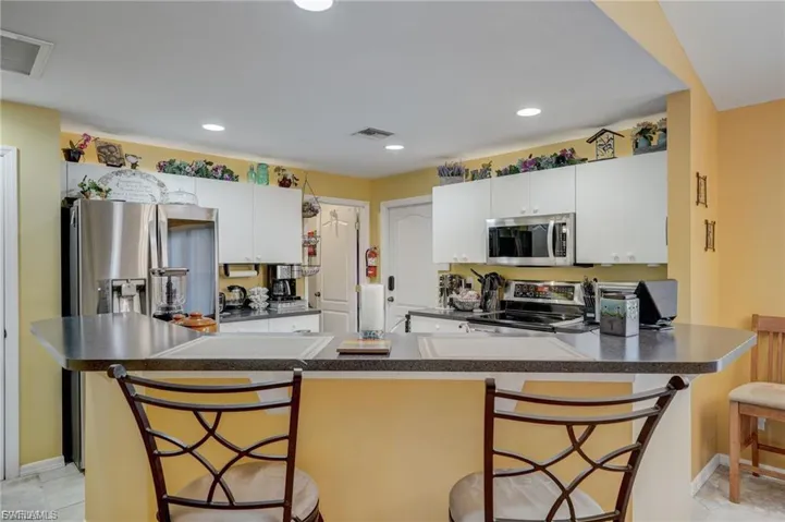 Kitchen with a kitchen breakfast bar, stainless steel appliances, dark countertops, white cabinets, and recessed lighting