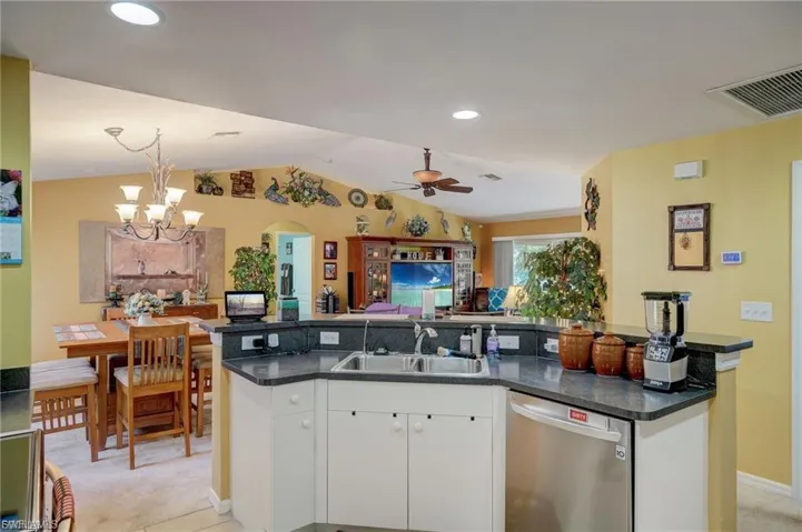 Kitchen featuring white cabinets, stainless steel dishwasher, a kitchen island with sink, open floor plan, and light carpet