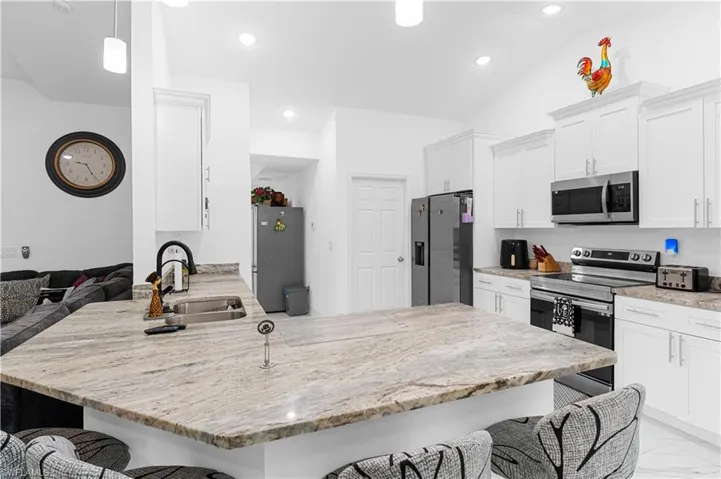 Kitchen featuring a breakfast bar area, a peninsula, appliances with stainless steel finishes, light stone counters, and recessed lighting