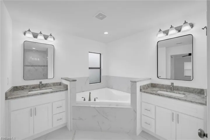 Full bathroom featuring two vanities, a bath, light marble finish floors, recessed lighting, and a marble finish shower