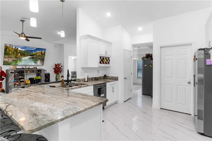 Kitchen with a peninsula, white cabinets, light stone countertops, pendant lighting, and stainless steel appliances