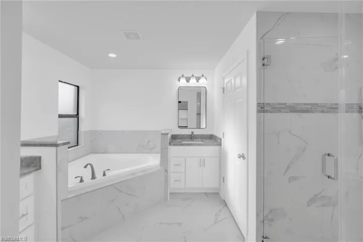 Full bathroom featuring a bath, vanity, light marble finish flooring, and a marble finish shower