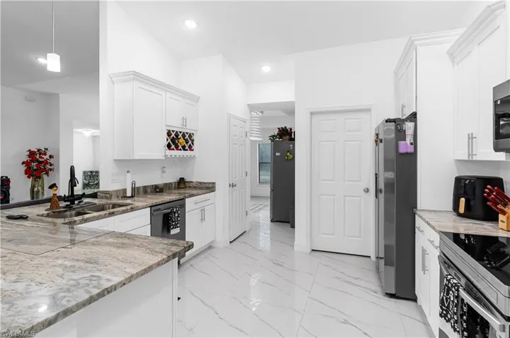 Kitchen featuring white cabinetry, appliances with stainless steel finishes, light marble finish flooring, hanging light fixtures, and light stone counters