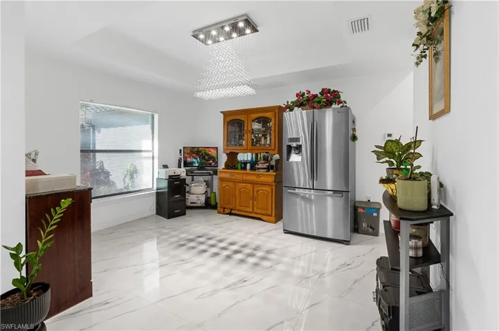 Kitchen with a tray ceiling, stainless steel fridge, brown cabinetry, and light marble finish floors