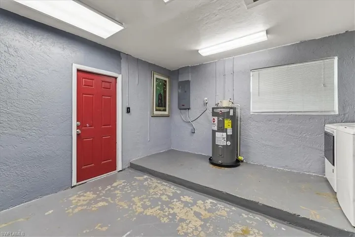 Below grade area featuring independent washer and dryer, water heater, electric panel, and a textured wall