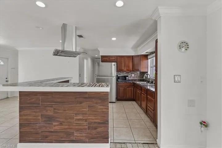 Kitchen featuring crown molding, island exhaust hood, light tile patterned floors, and appliances with stainless steel finishes