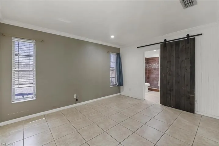 Spare room with a barn door, visible vents, recessed lighting, crown molding, and light tile patterned floors