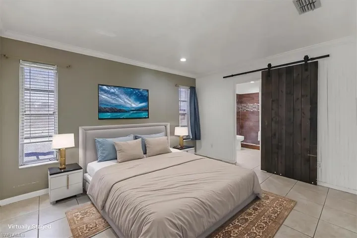 Bedroom with a barn door, light tile patterned floors, baseboards, visible vents, and crown molding