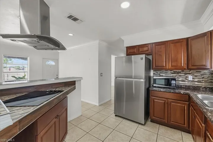 Kitchen with stainless steel appliances, ornamental molding, visible vents, island range hood, and backsplash