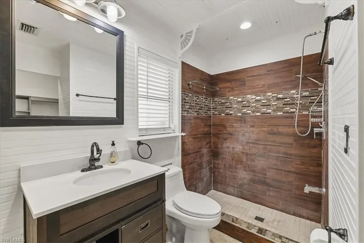 Full bath with toilet, a tile shower, visible vents, vanity, and recessed lighting