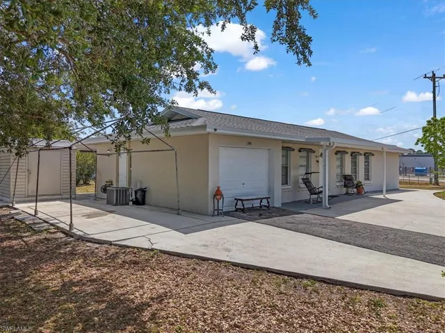 Rear view of house with cooling unit, stucco siding, concrete driveway, an outdoor structure, and a shed