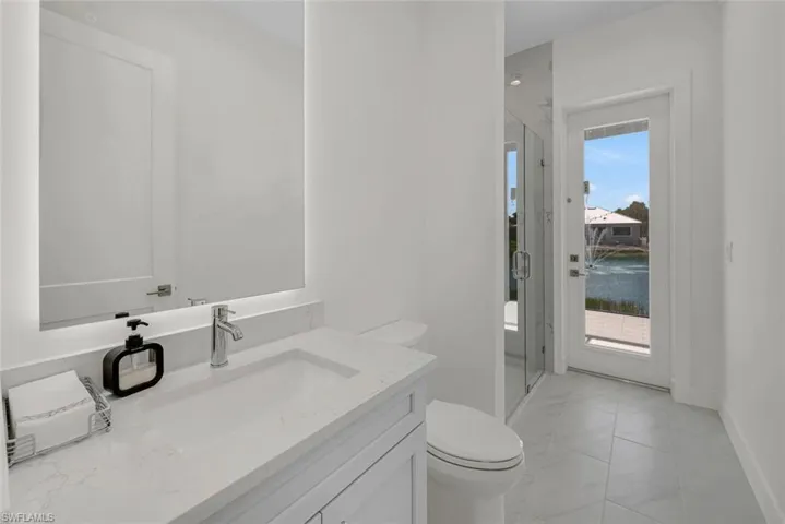 Pool Bath featuring walk in frameless glass shower, Quartz vanity top with a frameless, backlit, anti-fog mirror and tile patterned floor.