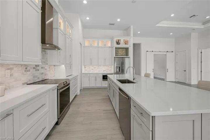 Kitchen featuring pullout spice, cookie sheet, utensil and shelving in base cabinets. Decorative lighted glass and SS designer hood. Modern Crown molding and oversized door and draw pulls.