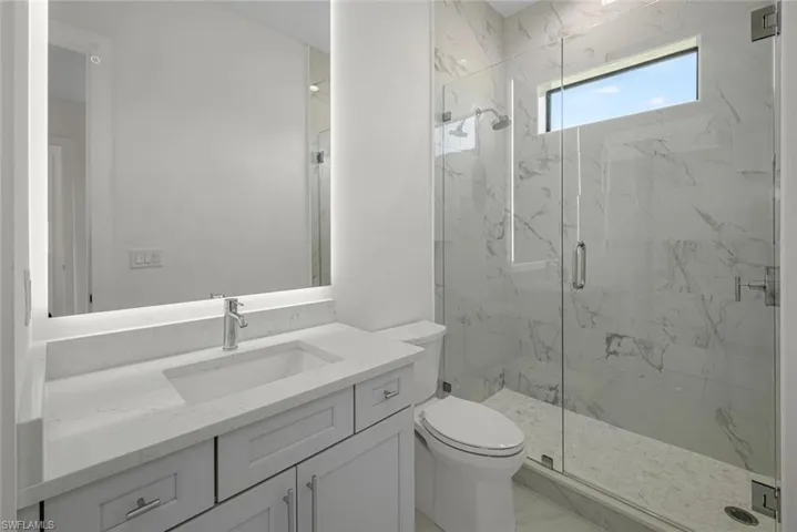 Second Bedroom Bath featuring Quartz vanity, backlit frameless anit-fog mirror, frameless shower enclosure and all custom tile work throughout.