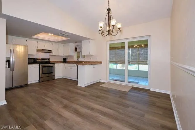 Kitchen with white cabinetry, stainless steel appliances, an inviting chandelier, sink, and dark wood-type flooring