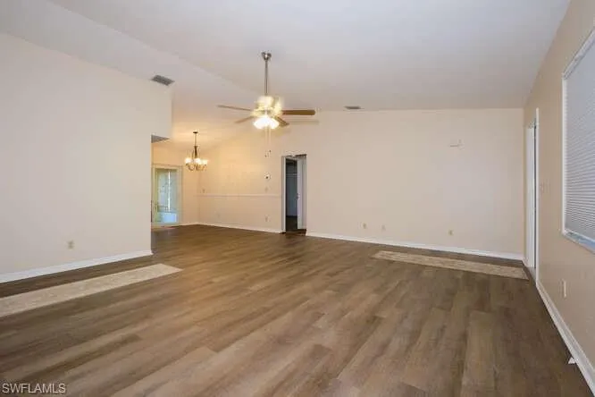 Unfurnished room with ceiling fan with notable chandelier, vaulted ceiling, and hardwood / wood-style floors