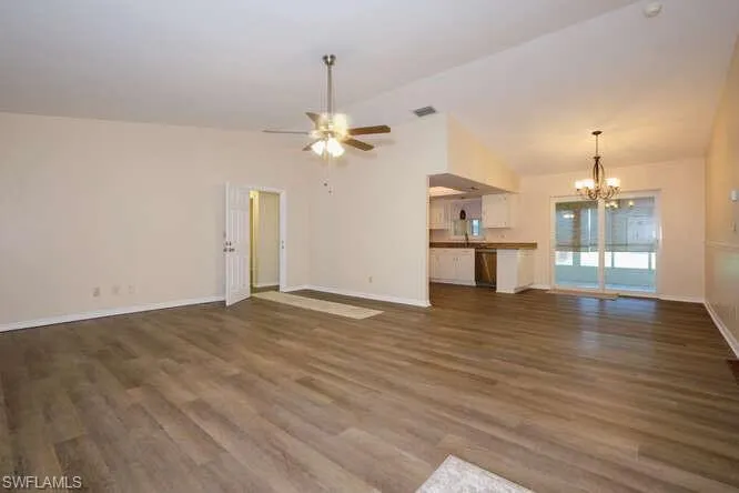 Unfurnished living room featuring dark hardwood / wood-style floors, ceiling fan with notable chandelier, and high vaulted ceiling