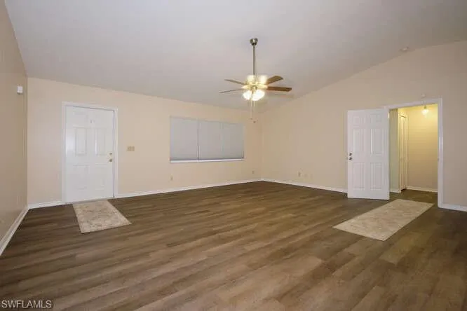 Unfurnished living room with dark wood-type flooring, ceiling fan, and vaulted ceiling