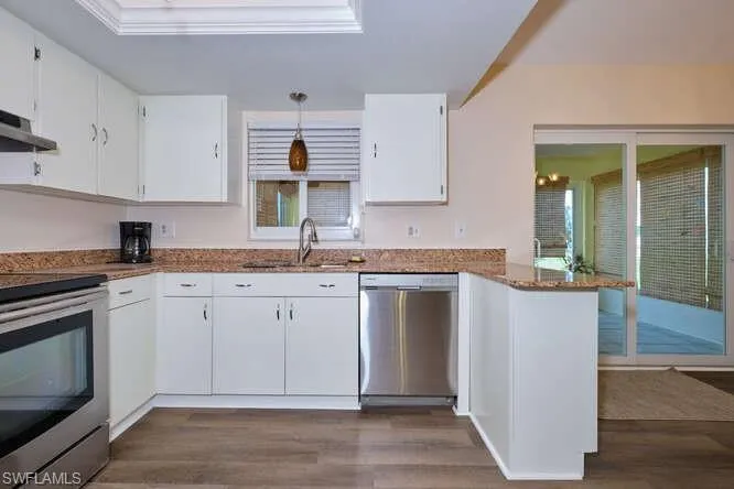 Kitchen with dark hardwood / wood-style floors, stainless steel appliances, sink, kitchen peninsula, and white cabinetry