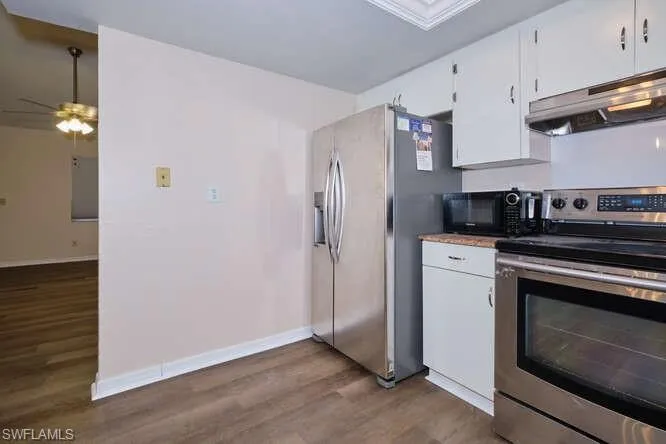 Kitchen with dark wood-type flooring, ceiling fan, appliances with stainless steel finishes, and white cabinets