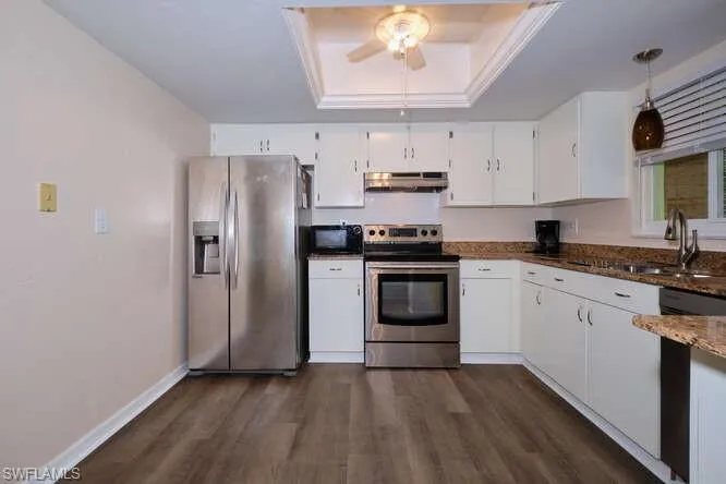 Kitchen featuring black appliances, ceiling fan, a tray ceiling, and dark wood-type flooring